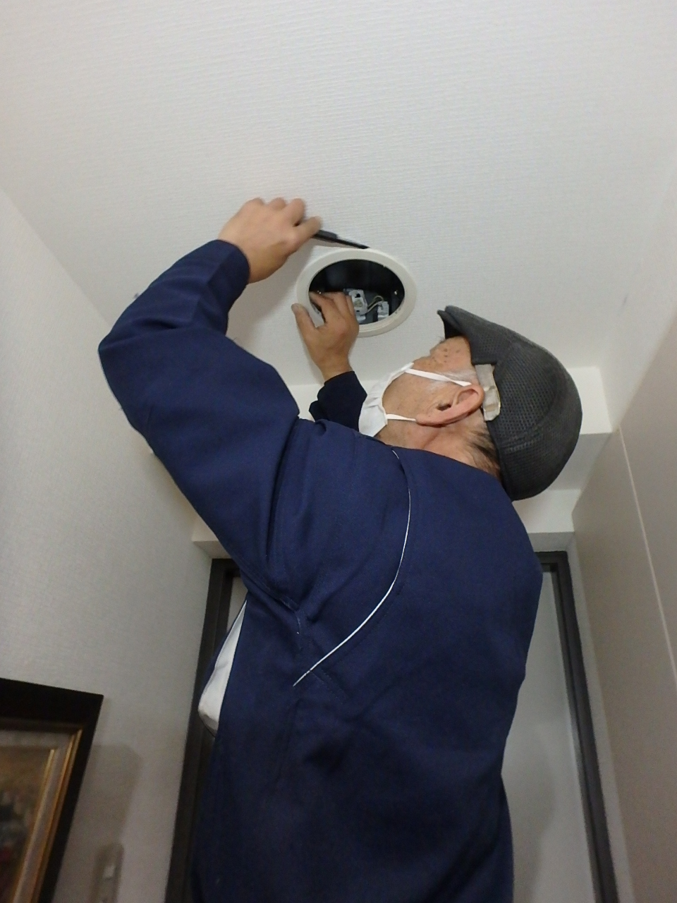 古いツイン蛍光灯からLEDへ、天井の開口部でダウンライトの交換・結線工事を行う電気工事職人