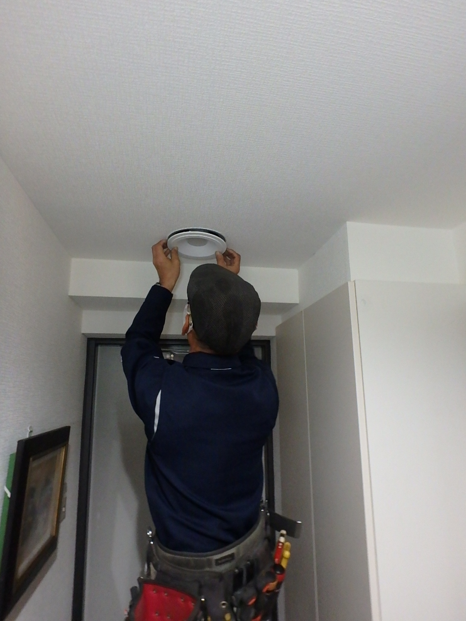 ホールカバーを組み込んだ新しいLEDダウンライトを、天井の開口部へ取り付ける職人の様子