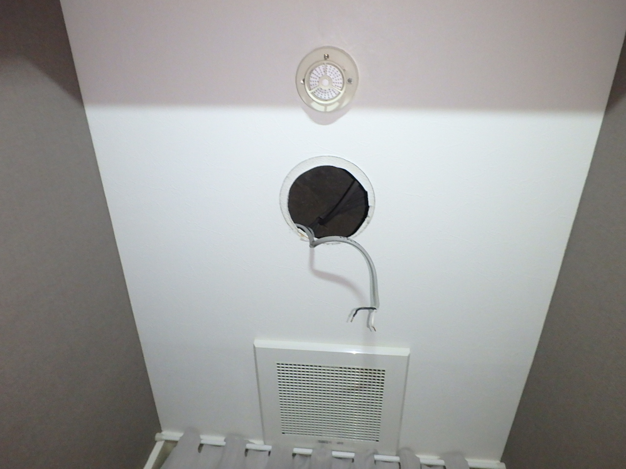 トイレの既存ダウンライトを外した天井の埋込穴。芯ズレにより、上側のクロス未施工部分の幅が広くなっている状態